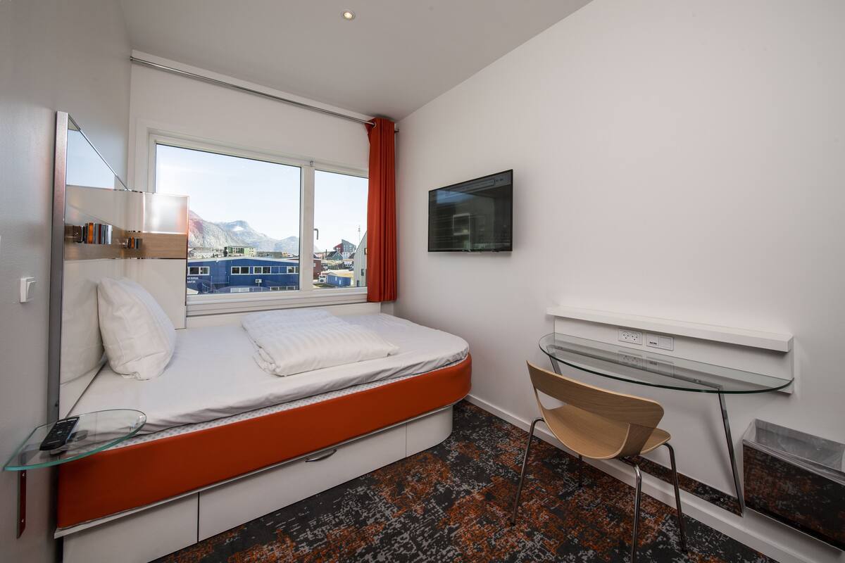 A modern hotel room with a bed, a glass table, a chair, and a TV.