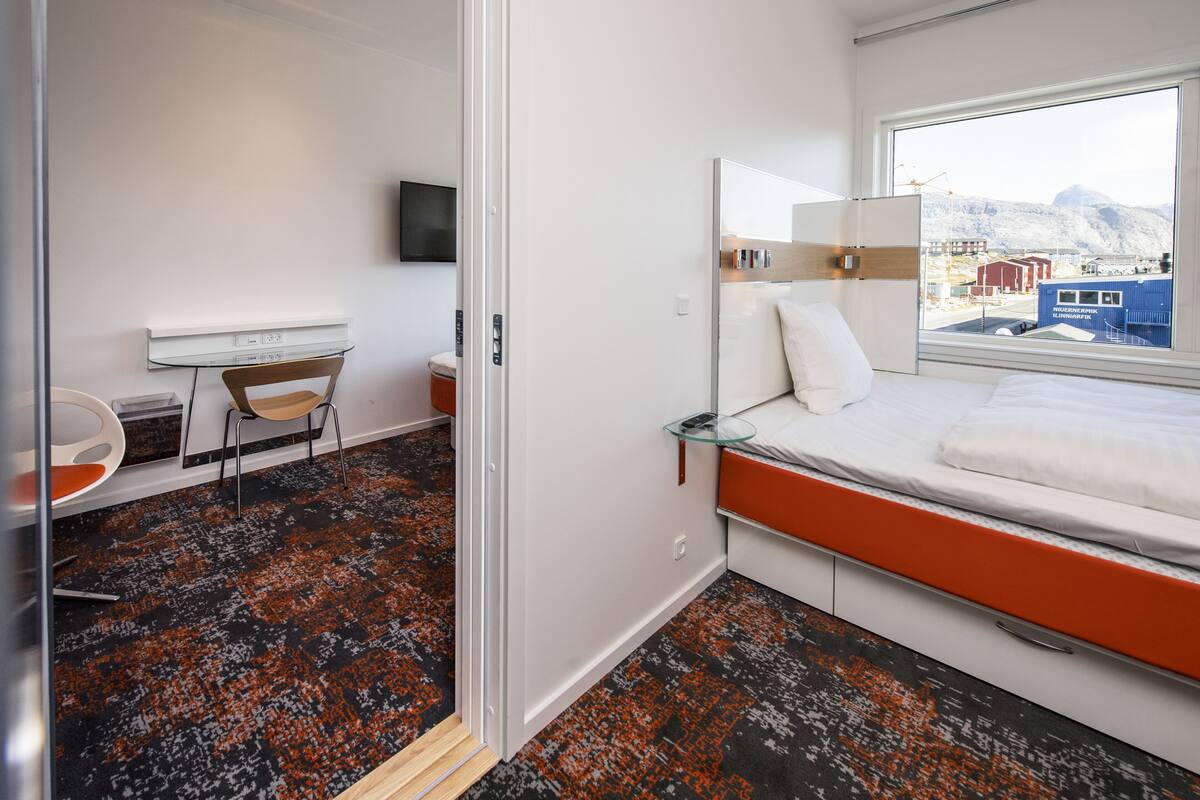 A modern hotel room with a bed, a desk, and a chair.