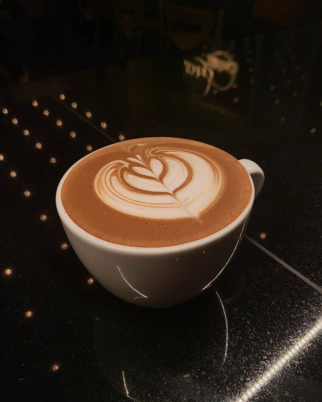 A cup of coffee with latte art on a dark surface.