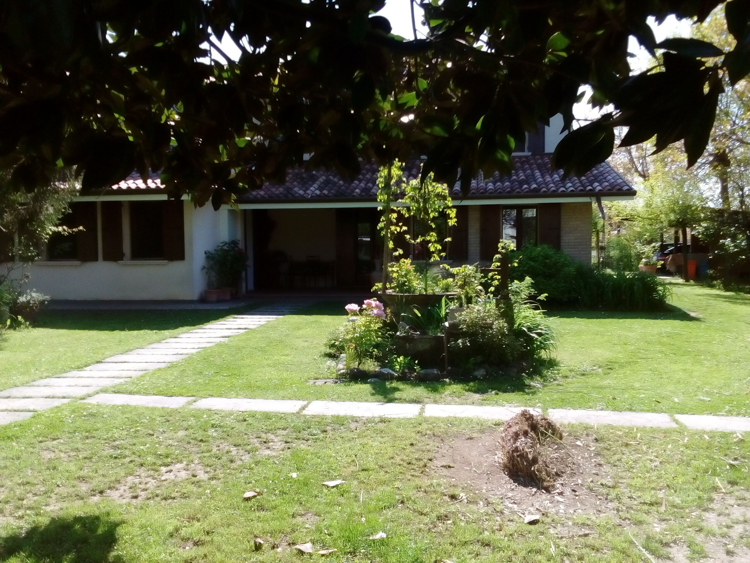 Una casa con techo de tejas, un porche delantero y un césped bien cuidado con un parterre de flores.