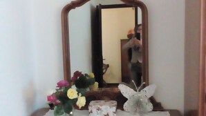 Un comò in legno con uno specchio, un vaso con fiori e un ornamento a forma di farfalla.