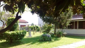 Un giardino con un vialetto in pietra, un pergolato e un edificio con tetto rosso.