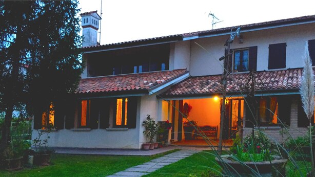 Una casa a due piani con tetto in tegole, un camino ben visibile e un giardino curato con un vialetto che conduce all'ingresso.