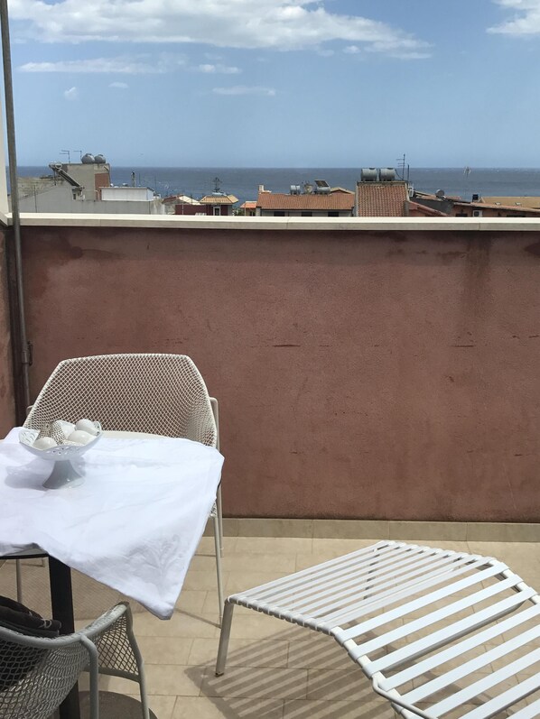 Un balcón con mesa y sillas, con vista a la costa, edificios y el mar.