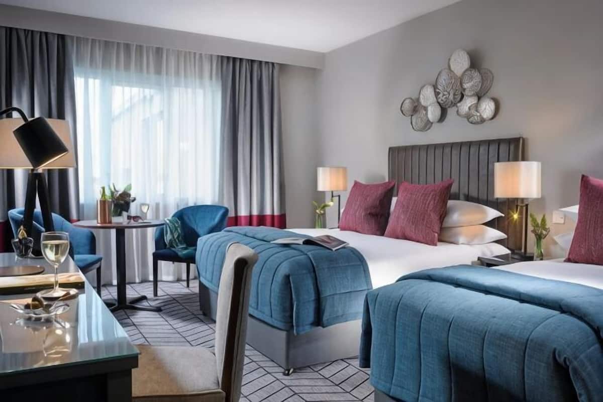 A hotel room with a bed, two bedside tables, a desk, a chair, and a window with curtains.