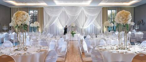 A banquet hall with round tables, white drapery, and tall floral arrangements.