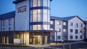 Et moderne hotel med en buet glasfacade, et skilt der viser Fairways Hotel, og en tydelig indgang.
