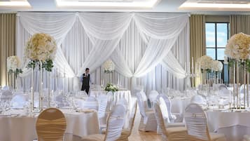 Une salle de banquet avec des tables rondes, des tentures blanches et de grandes compositions florales.