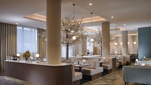 En moderne restaurant med central bar, siddepladser og dekorative træer.