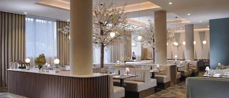 A modern restaurant with a central bar, seating areas, and decorative trees.