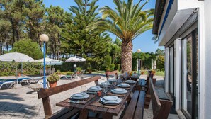 Un espace de restauration en plein air avec des tables en bois dressées pour le repas, entouré de plantes en pot et de parasols.