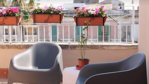 Varanda com duas cadeiras e três vasos suspensos com flores cor-de-rosa.