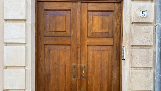 Uma porta de madeira dupla com um pequeno degrau que a precede, em um edifício de pedra.