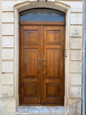 Une porte en bois à deux battants, précédée d’un petit seuil, est intégrée à un bâtiment en pierre.