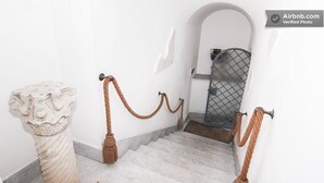 Uma escadaria de mármore com guarda-corpo de corda, parede branca e portão de metal ao fundo.