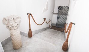 A marble staircase with a rope barrier, a white wall, and a metal gate in the background.
