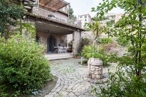 Un patio de piedra con una mesa y sillas, rodeado de follaje y un pilar de piedra.