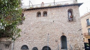 Um edifício de pedra com uma porta arqueada central, três pequenas janelas e uma varanda com guarda-corpo.