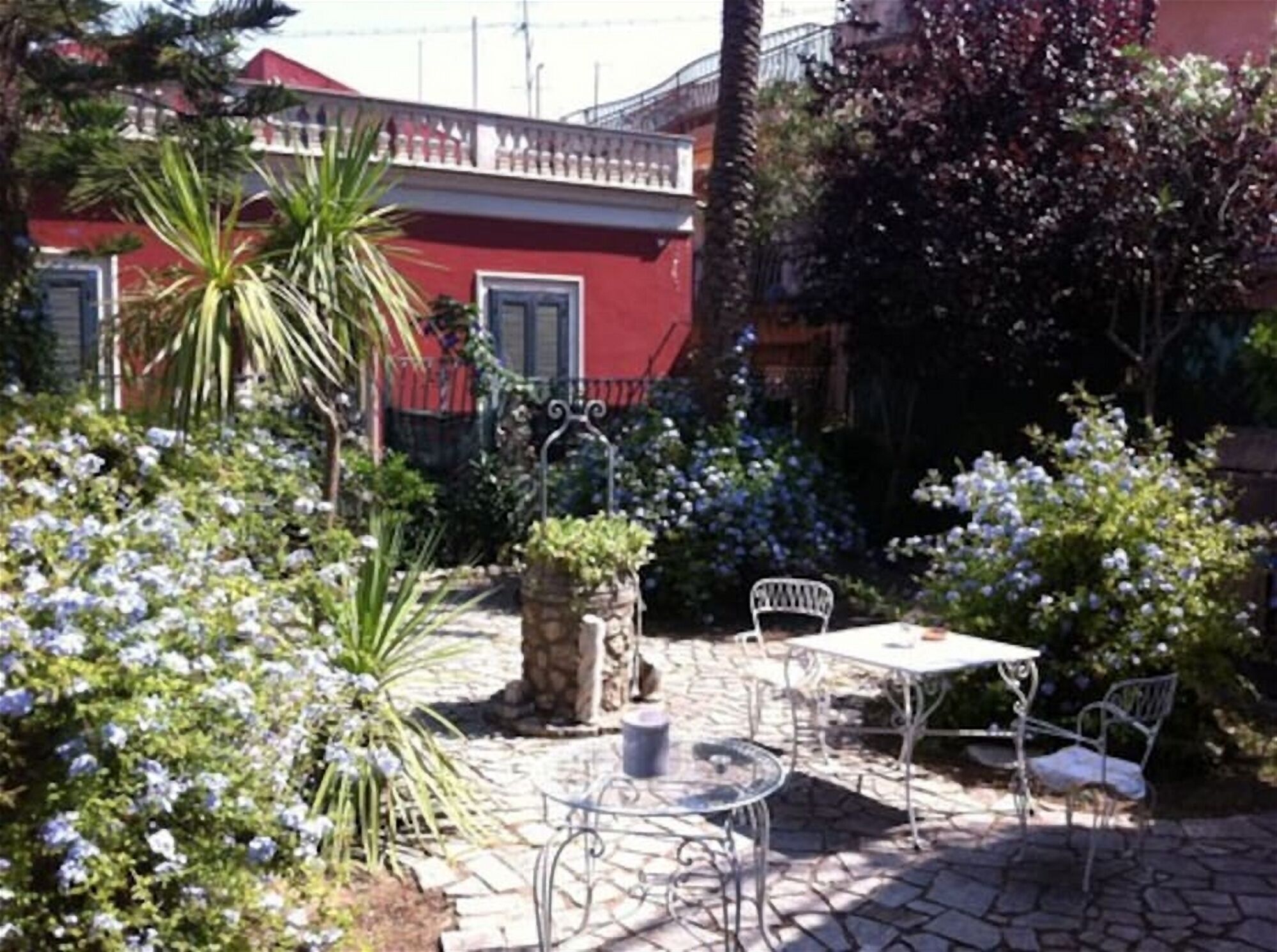 A courtyard with a stone floor, a table with chairs, and a variety of plants and flowers.
