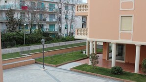 A courtyard with a paved walkway, a small lawn, and a building with balconies and a covered entrance. - Geranei Appartamento Bilocale a 50 metri dal mare (TAGGIA)