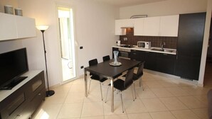 A modern kitchen with white cabinets, a black countertop, and a dining area with a table and chairs. - Geranei Appartamento Bilocale a 50 metri dal mare (TAGGIA)