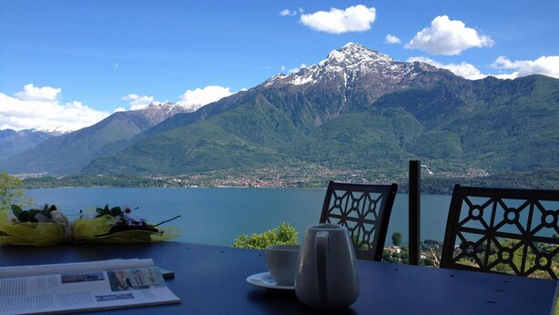 Une table avec un journal, une tasse et un vase, donnant sur un lac avec des montagnes en arrière-plan.