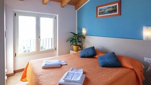 Une chambre à coucher avec un lit, des oreillers, une plante en pot, une fenêtre et un tableau accroché au mur.