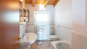 Une salle de bain avec un plafond en bois, un lavabo blanc, des toilettes et une baignoire.