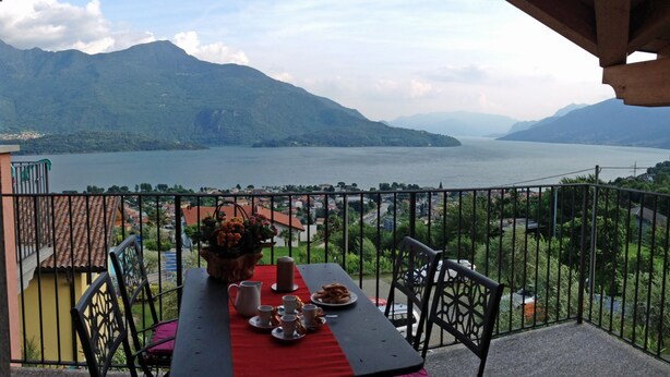 Un balcon avec une table dressée pour deux personnes, offrant une vue sur un lac et des montagnes.