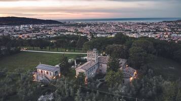 A panoramic view of a cityscape at dusk with a prominent historical building surrounded by greenery.