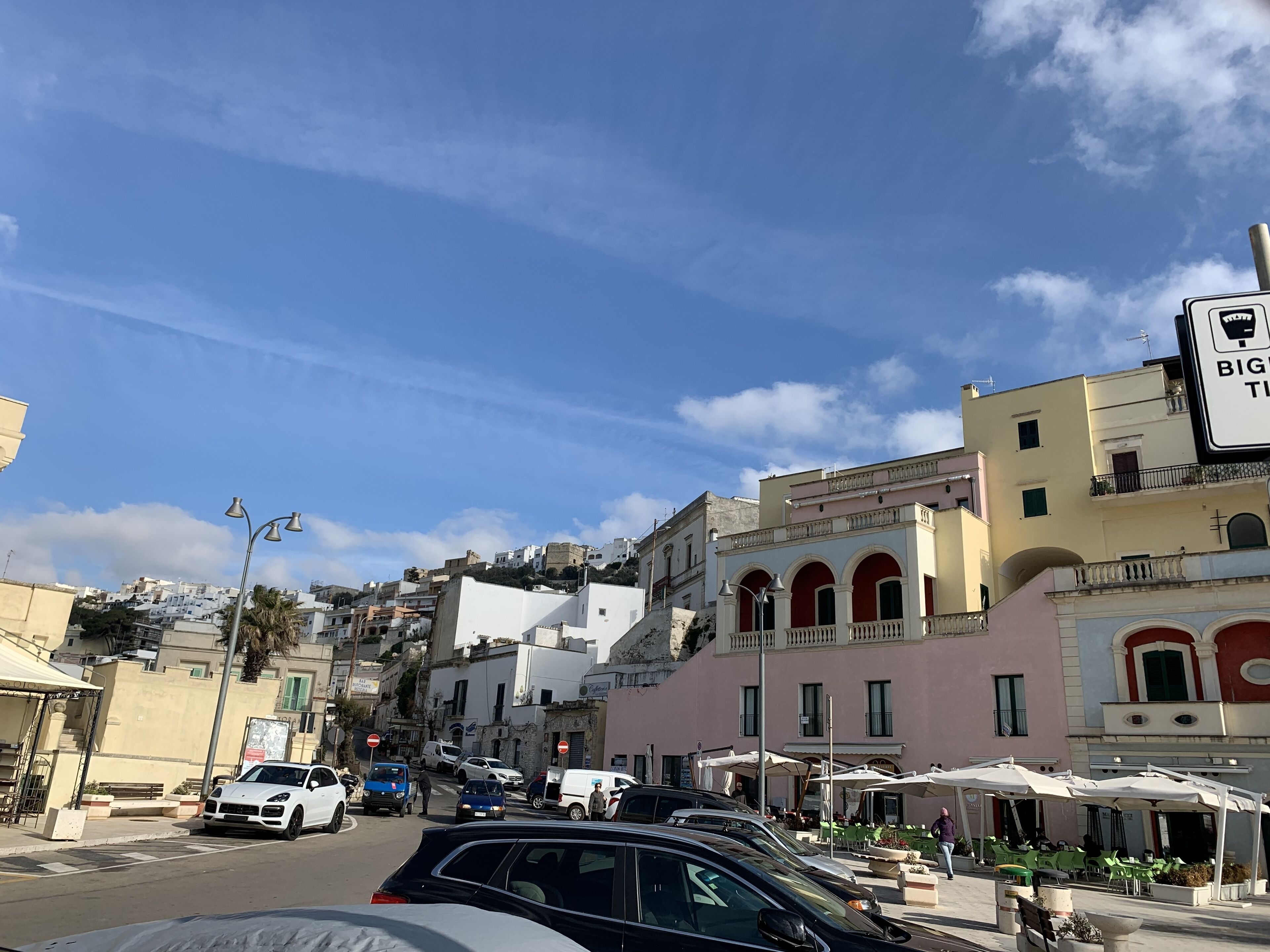 A street with parked cars, buildings, and outdoor seating areas.