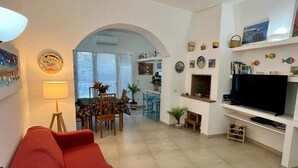 Un salon avec un canapé rouge, un téléviseur et une cheminée. On y trouve également un coin repas avec des chaises et une table.