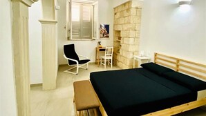 Une chambre avec un lit en bois, un bureau, une chaise et un mur en pierre.