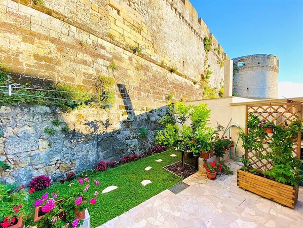 A courtyard with a stone wall, a small garden with artificial grass and potted plants, and a wooden fence. - PRICELESS RESIDENCE in the ANCIENT VILLAGE of CASTRO MARINA (LE) (Castro Marina)
