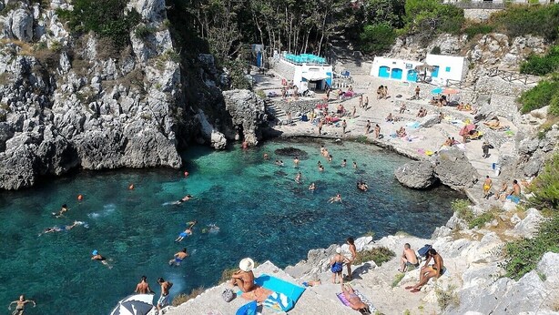 Une zone côtière aménagée pour la baignade, avec un terrain rocheux et un petit bâtiment aux portes bleues.