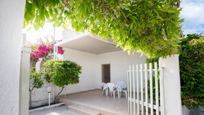 A covered patio area with a white fence, a small table with chairs, and potted plants.