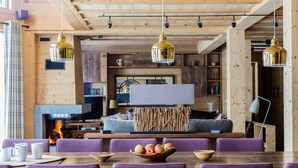 Ein gemütliches Blockhaus-Interieur mit Kamin, Holzwänden und einer Essecke mit violetten Stühlen.