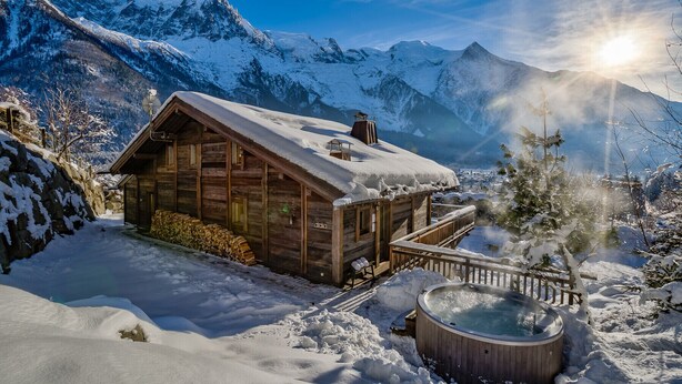 Eine Holzhütte mit Whirlpool in einer verschneiten Berglandschaft.