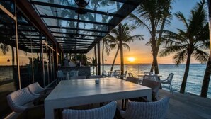 An outdoor dining area with a table and chairs, overlooking a body of water with palm trees.