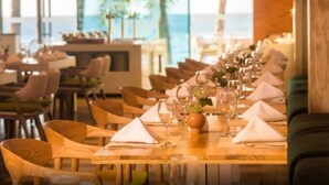 A restaurant with wooden tables and chairs, arranged in a row with a view of the ocean.