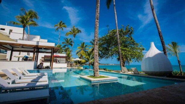 A pool area with lounge chairs, palm trees, and a view of the ocean.