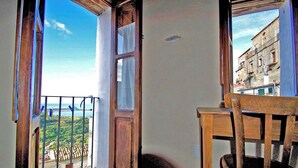 A balcony with a wooden chair, a table, and a view of a cityscape and greenery. - Characteristic house in the historic centre of Belmonte Calabro, Nature and Culture (Belmonte Calabro)