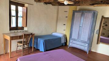 A small room with a wooden desk, a bed with a blue bedspread, a wardrobe, and a window with curtains.