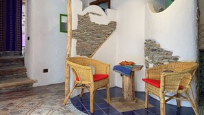 A room with two wicker chairs, a small table with a blue cloth, and a stone wall. - Characteristic house in the historic centre of Belmonte Calabro, Nature and Culture (Belmonte Calabro)
