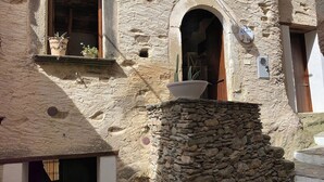 A rustic stone building with a stone staircase leading to a door, a window with a wooden shutter, and a small shelf with potted plants. - Characteristic house in the historic centre of Belmonte Calabro, Nature and Culture (Belmonte Calabro)