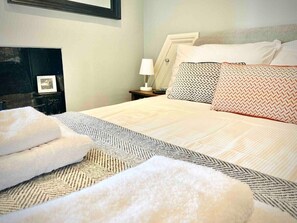A neatly made bed with a patterned bedspread, two pillows with geometric designs, and a bedside lamp.