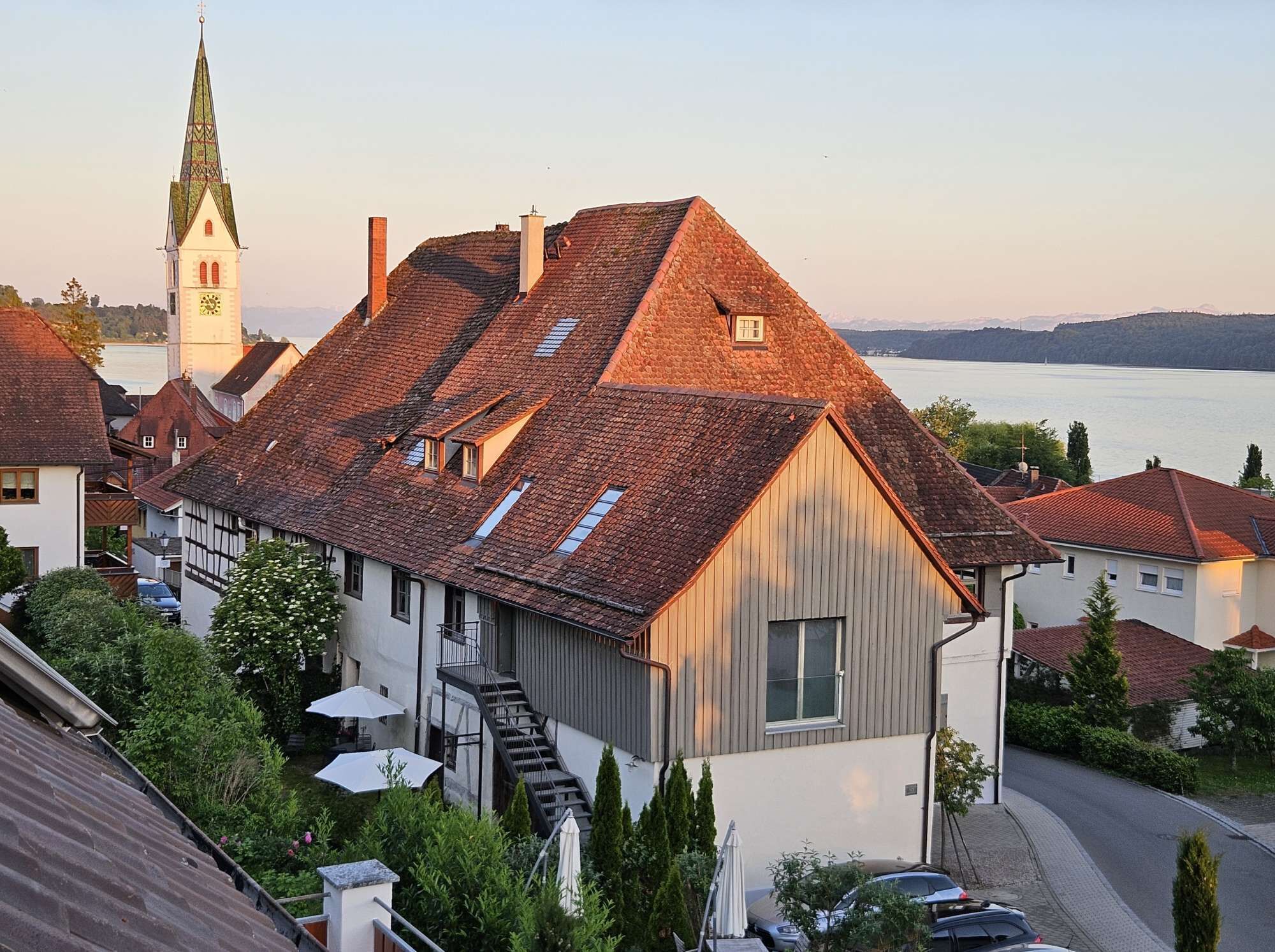 Ein traditionelles Gebäude mit einem steilen Dach, einer sichtbaren Treppe und Blick auf ein Gewässer im Hintergrund.