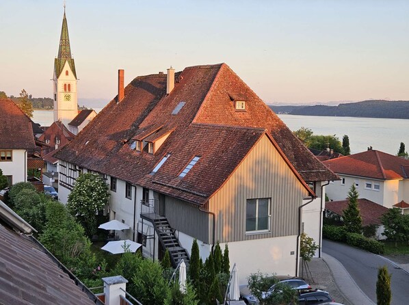 A traditional building with a steep roof, a visible staircase, and a view of a body of water in the background.
