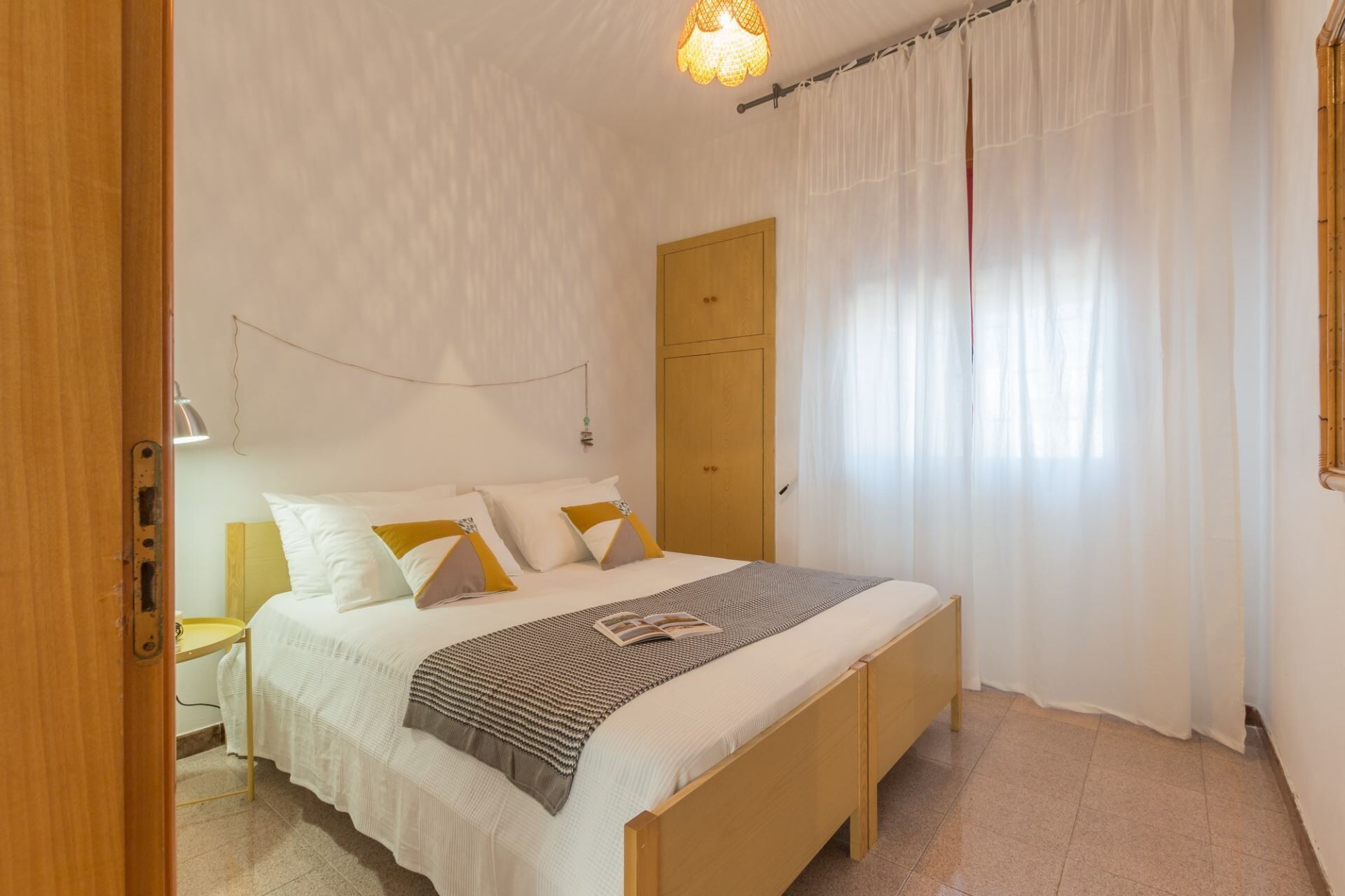 A bedroom with a wooden bed, white bedding, a bedside table with a lamp, and a wooden wardrobe.