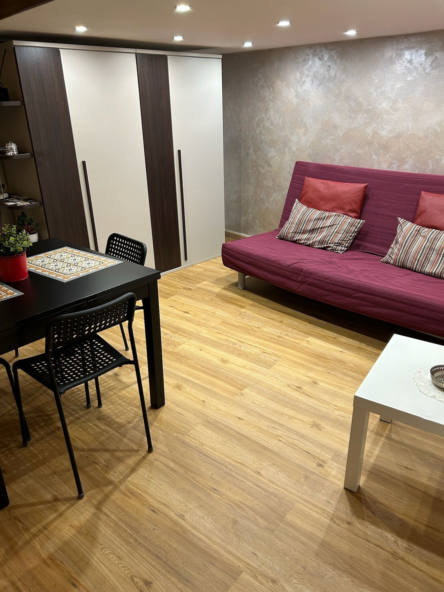 Un salon moderne avec un plancher en bois, une table à manger avec des chaises, un canapé avec des coussins et une table basse blanche.